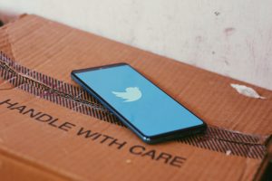 Image of a mobile phone showing the twitter logo on a box that says 'handle with care'