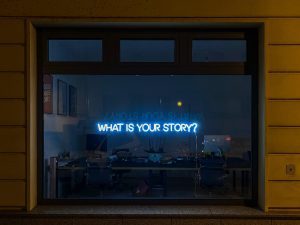 A neon sign with the words 'what's your story?'