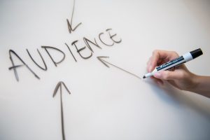 Photo of a person's hand writing the word "audience" on a whiteboard, with arrows.