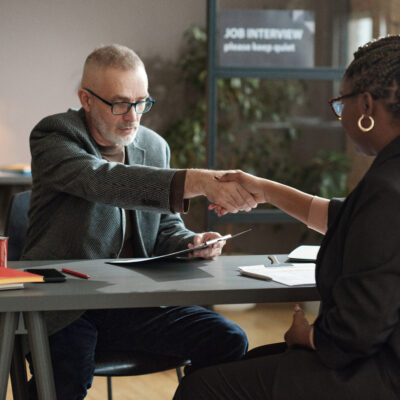 Mature manager shaking hands with young woman while they sitting at table during job interview